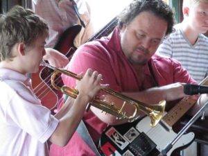 Jason Vivone with guitar watches a child play a trumpet