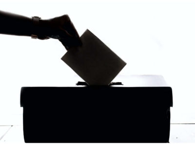 image of a hand putting a ballot into a box