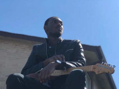 Mathias Lattin poses with guitar and a blue sky background