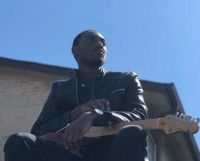 Mathias Lattin poses with guitar and a blue sky background
